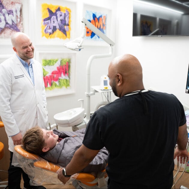 Dr. Greg Gelfand and a dental assistant consulting with a young male patient in a modern dental exam room.